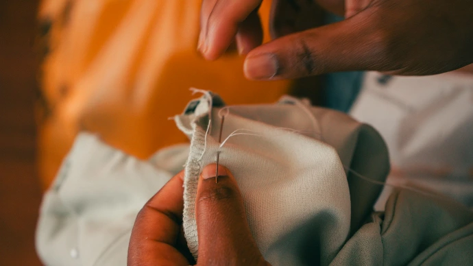 Hands sewing light fabric with a needle and thread.